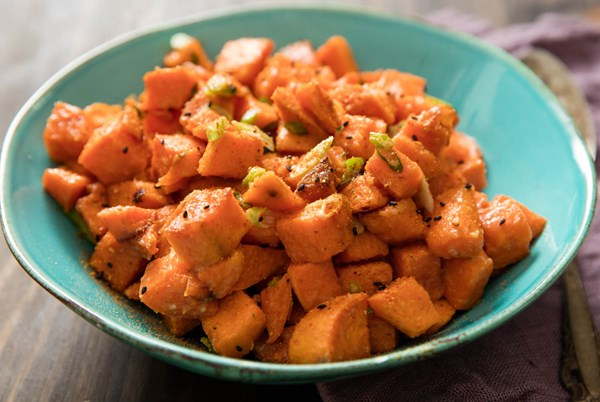 A blue-green bowl holds cooked, diced orange fleshed sweet potatoes dotted with tiny black black seeds and bits of scallion